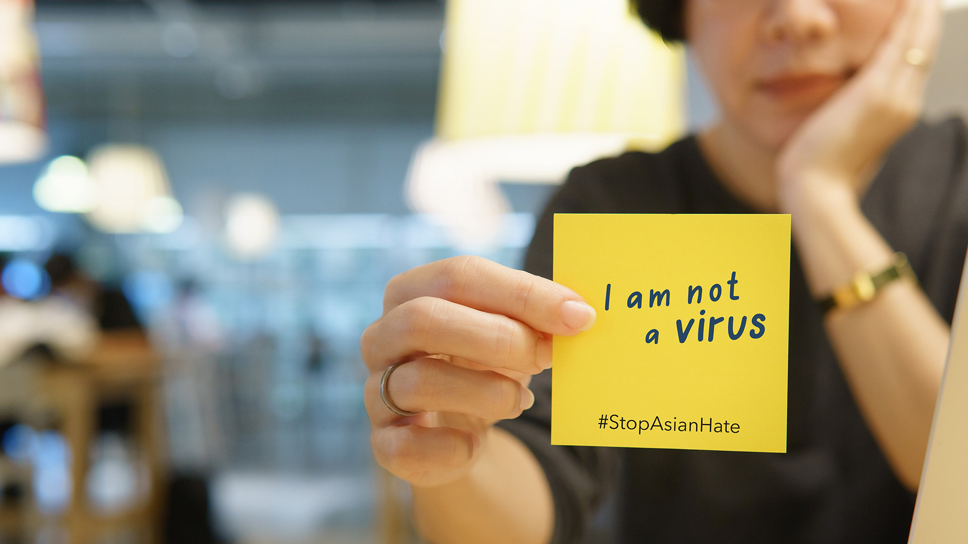 A blurred woman holds a note with the words I am not a virus, #StopAsianHate