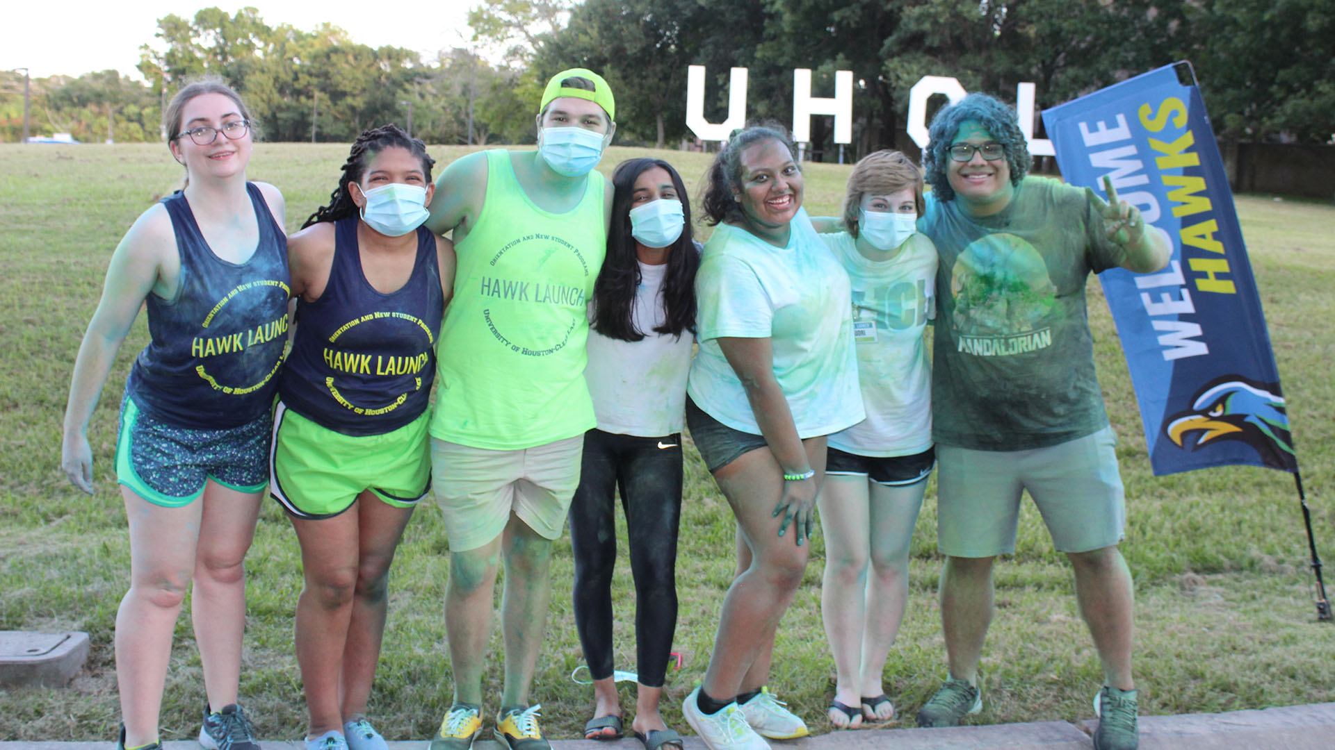 Students covered in colors from a game gathered in front of the UHCL letters