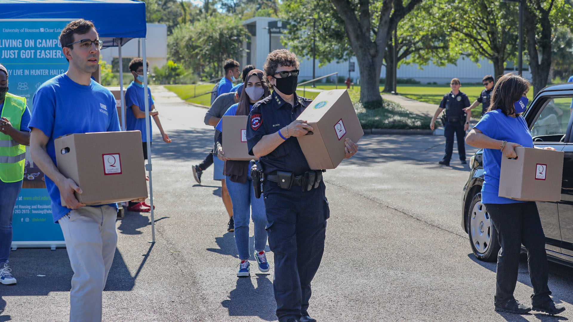 Volunteers in UHCL shirts carry boxes of food to a waiting vehicle