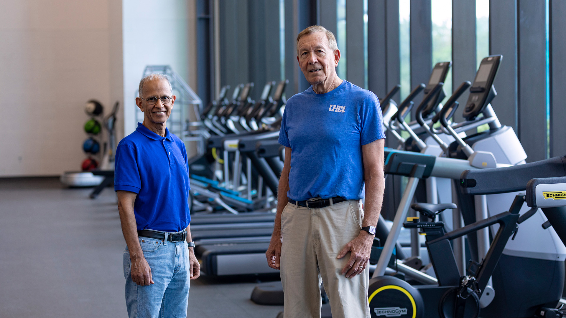 Two men in blue shirts standing among exercise equipment